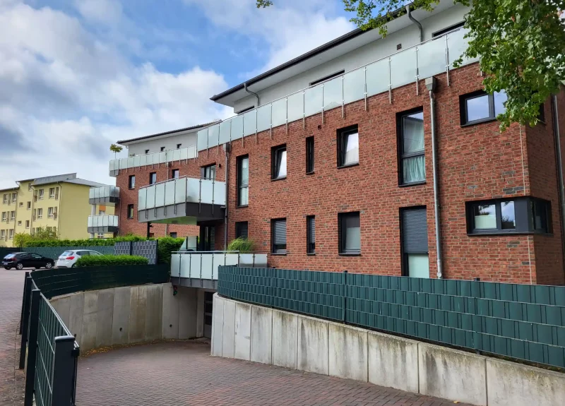 Mehrfamilienhaus mit Klinkerfassade, Balkon mit Edelstahlgeländer und Einfahrt in eine Tiefgarage