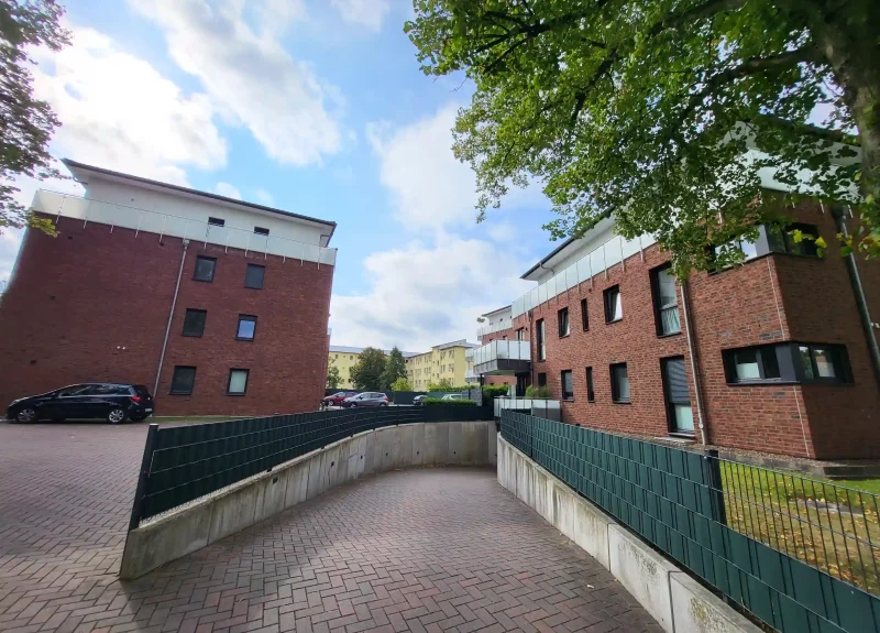 Mehrfamilienhaus mit Klinkerfassade, Balkon mit Edelstahlgeländer und Einfahrt in eine Tiefgarage